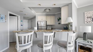 Une cuisine avec des armoires blanches, un comptoir en granit et trois chaises blanches.