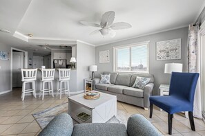 Un soggiorno con un divano grigio, una poltrona blu, un tavolino da caffè bianco e una ventola a soffitto.