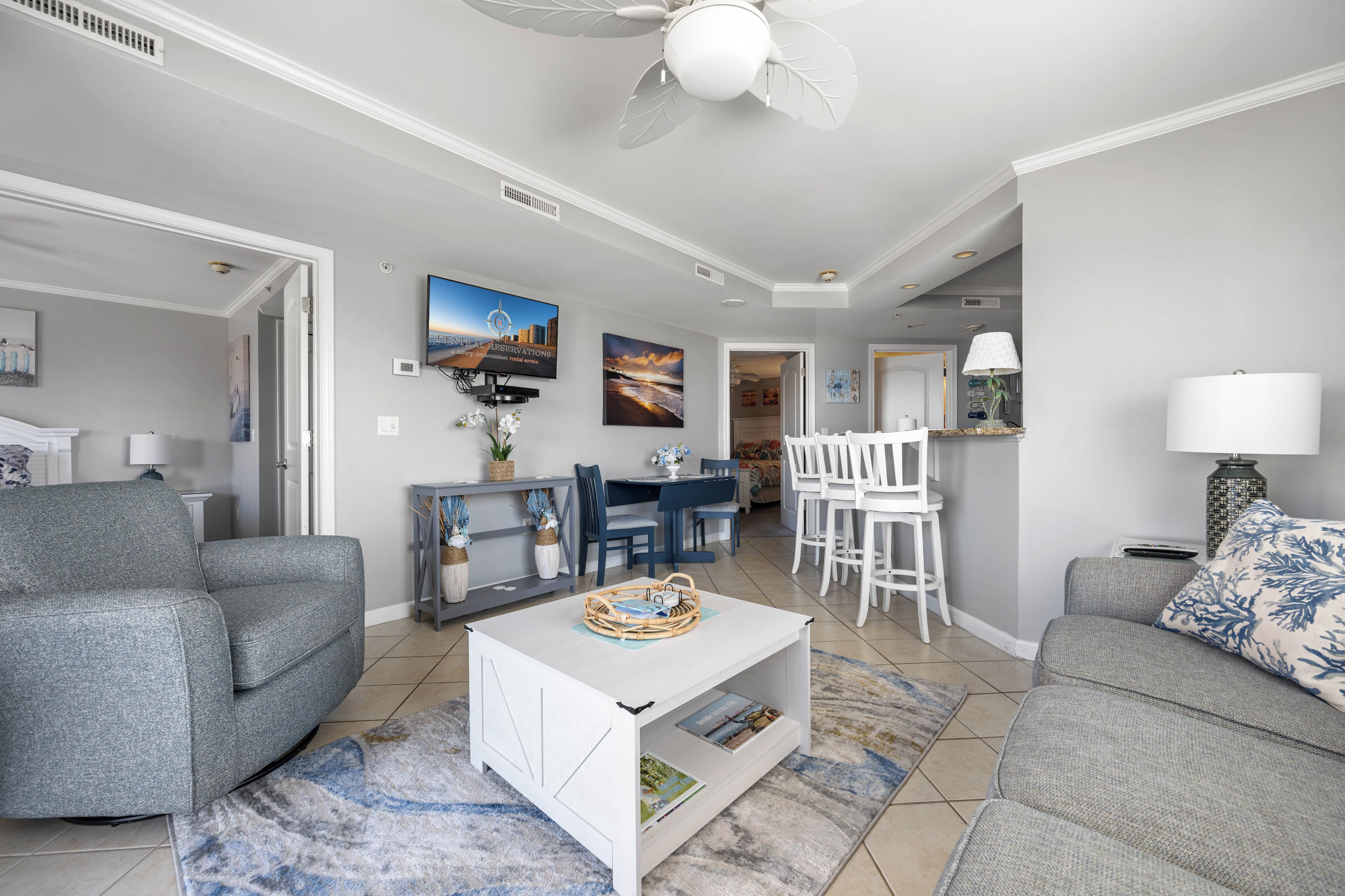 A living room with a sofa, a coffee table, a TV, a dining area with chairs, and a ceiling fan.