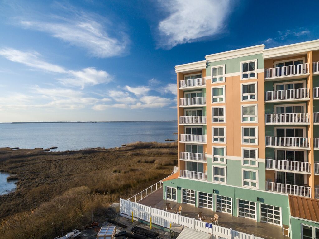 A multi-story hotel with balconies, a view of the beach, and a parking area.