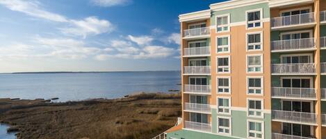 A multi-story hotel with balconies, a view of the beach, and a parking area.