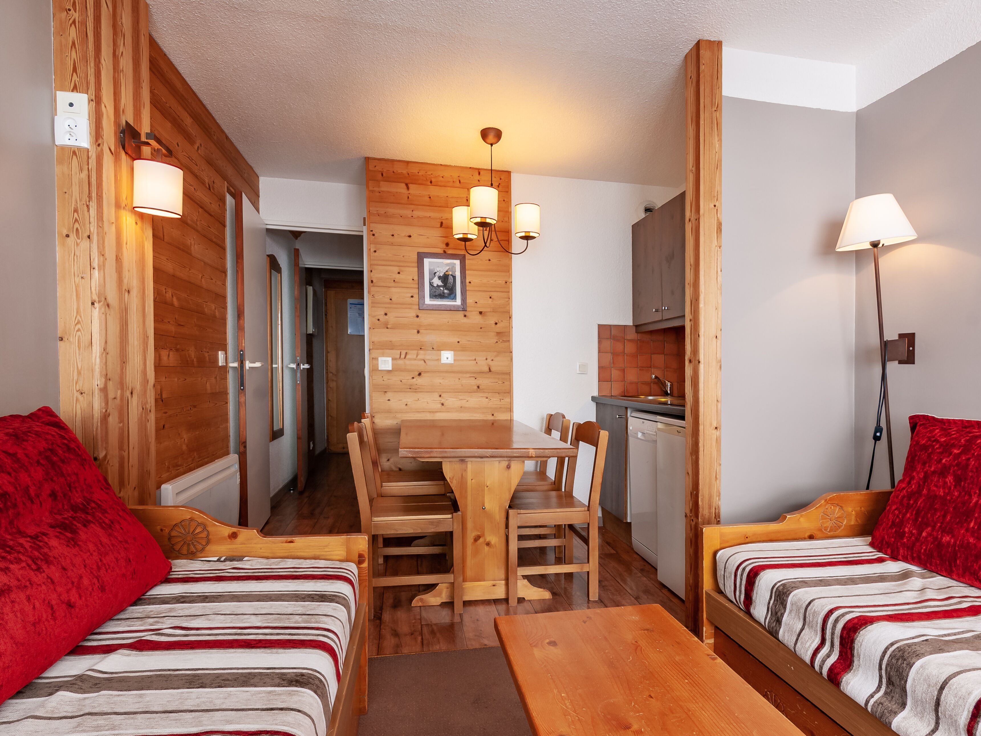 A compact room with two beds, a wooden dining table, and a kitchenette.
