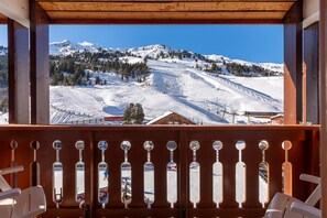 Un balcon en bois offrant une vue sur une montagne enneigée et des pistes de ski.