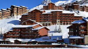 A ski resort with multiple wooden buildings, including a restaurant and a bar, surrounded by snow-covered mountains. - Résidence Le Pralin - Méribel-Mottaret (Les Allues)