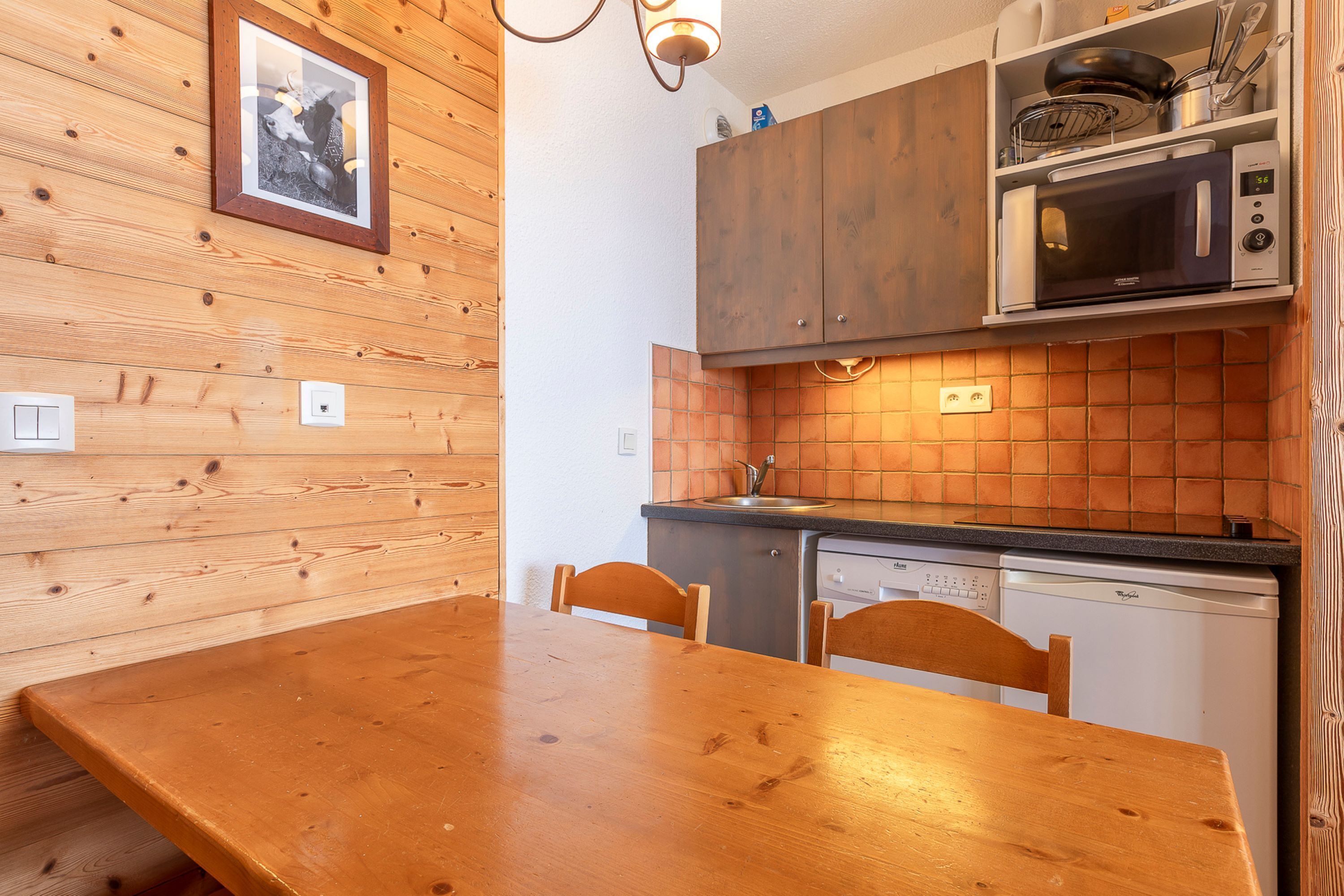 Ein Holzespeise-Tisch mit Stühlen, eine Küche mit Mikrowelle, Geschirrspüler und Holzschränken.