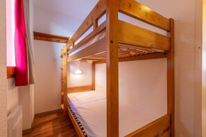 Une chambre avec un lit superposé, une structure en bois, un matelas blanc et un luminaire au plafond.