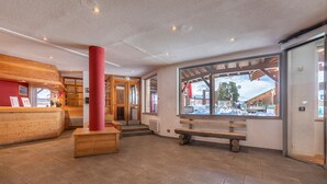 A reception area with a wooden desk, a red pillar, and a bench. - Résidence Le Pralin - Méribel-Mottaret (Les Allues)