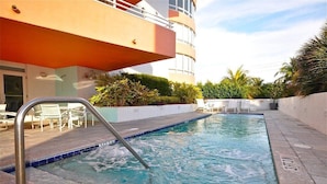 A swimming pool with a metal ladder, surrounded by a white wall and greenery.