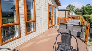 Une maison dotée de grandes fenêtres, d’une terrasse en bois et de mobilier d’extérieur.