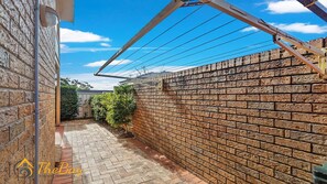 A brick wall with a metal structure, a paved pathway, and a clear blue sky. - Moy at Nelson Bay - 2/30 Thurlow Avenue (Nelson Bay)
