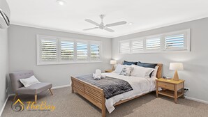 A bedroom with a bed, two bedside tables, a chair, a ceiling fan, and windows with blinds. - Moy at Nelson Bay - 2/30 Thurlow Avenue (Nelson Bay)