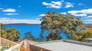 A coastal view with a clear sky, a large tree in the foreground, and a distant shoreline. - Moy at Nelson Bay - 2/30 Thurlow Avenue (Nelson Bay)