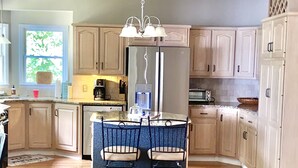 Une cuisine avec des meubles en bois, un îlot central doté de chaises, un réfrigérateur et un luminaire suspendu.