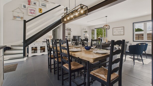 Een moderne eethoek met een houten tafel, zwarte stoelen en een trap naar een hoger niveau.