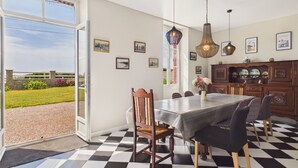 Un comedor con piso a cuadros, una mesa con sillas, lámparas colgantes y cuadros en la pared.