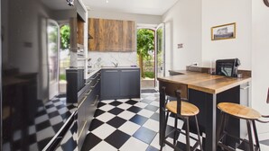 Una cocina moderna con piso a cuadros blancos y negros, gabinetes de madera, una barra con taburetes y vistas al exterior.