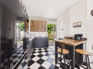 A modern kitchen with black and white checkered flooring, wooden cabinets, a bar area with stools, and a view of the outdoors.