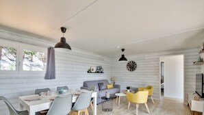 Ein modernes Wohnzimmer mit Essbereich, ausgestattet mit einer Couch, Sesseln, einem Couchtisch und einem Fernseher.