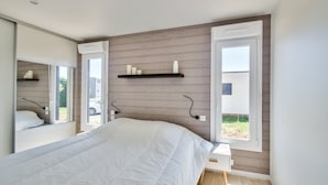 Ein modernes Schlafzimmer mit einem großen Bett, einem Nachttisch, einem Spiegel und einem Fenster mit Vorhängen.