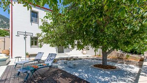 Eine Terrasse mit Liegestühlen, einem kleinen Baum und einem weißen Gebäude mit rotem Dach.