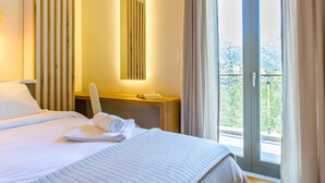 Ein Hotelzimmer mit einem großen Bett, einem Schreibtisch, einem Spiegel und einem Balkon mit Vorhängen.