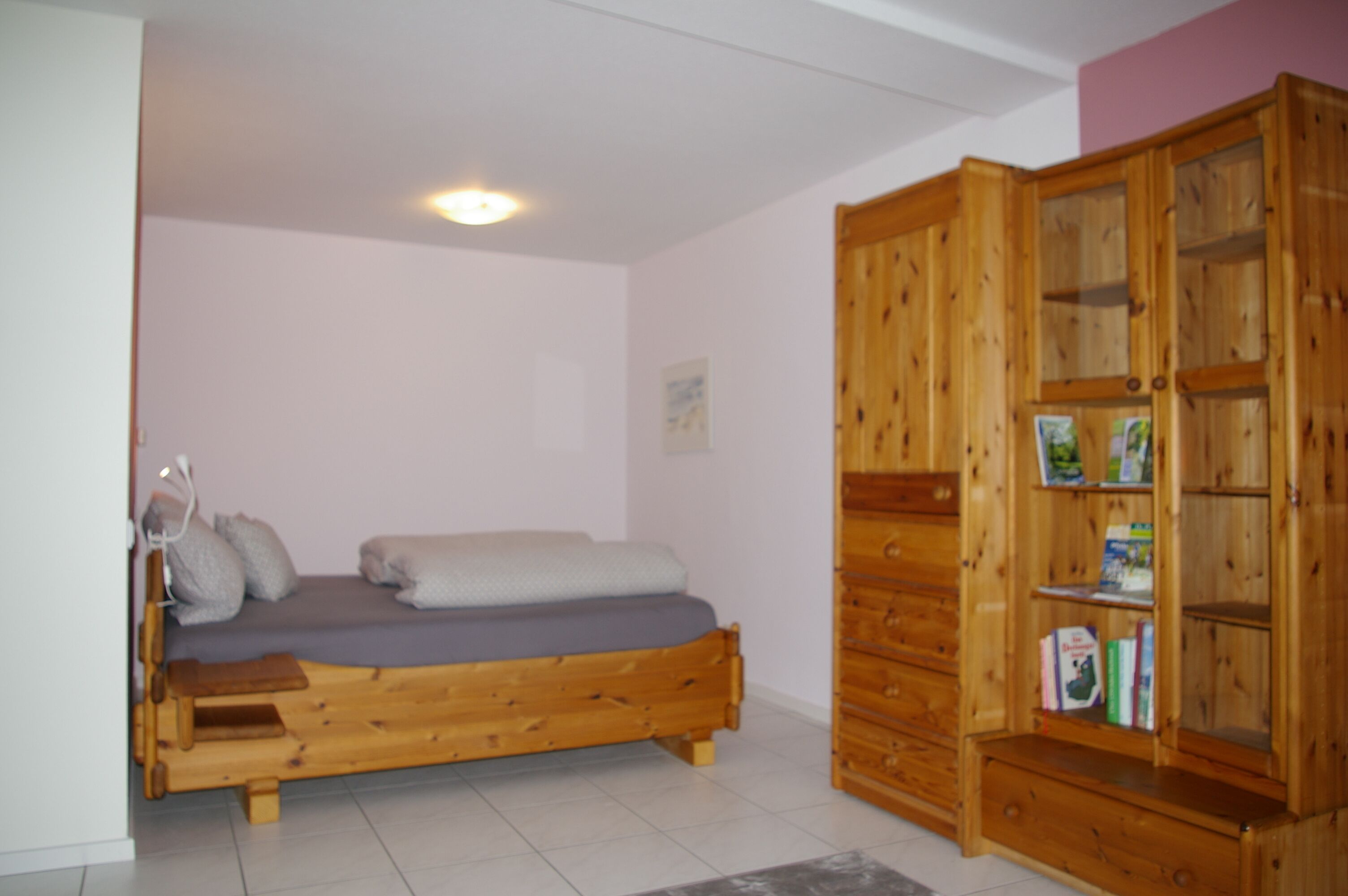Ein Zimmer mit einem hölzernen Bett, einem Holzschrank und einer kleinen Bank.