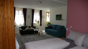 A living room with a bed, a blue sofa, a black sofa, a small table, and a plant. - Im Alten Löwen (Hochstadt (Pfalz))