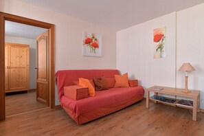 A cozy room with a red sofa, wooden cabinet, and a small table with a lamp.