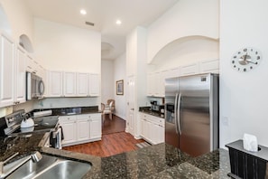 A modern kitchen with white cabinets, granite countertops, stainless steel appliances, and a clock on the wall.