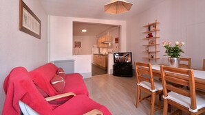 Un accogliente soggiorno con un divano rosso, un tavolo da pranzo con sedie, una TV e una cucina sullo sfondo.