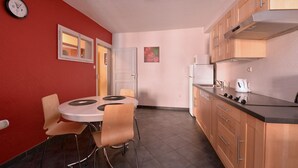 Una cucina compatta con zona pranzo, che include un tavolo rotondo con sedie, un frigorifero, un fornello e pensili in legno.