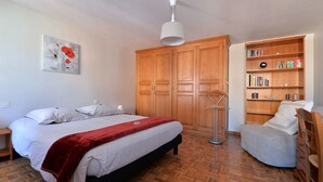 Ein Schlafzimmer mit Bett, Nachttisch, Holzschrank, Bücherregal und einer Stehlampe.