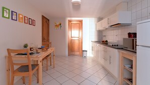 Eine kleine Küche mit weißen Schränken, einem Holztisch und einem Fliesenboden.