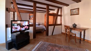 A room with exposed wooden beams, a bed, a television, a dining table with a chair, and a rug. - Gîtes du Couvent, "Schlossberg" beautiful apartment in the historic center of Kaysersberg (Kaysersberg)