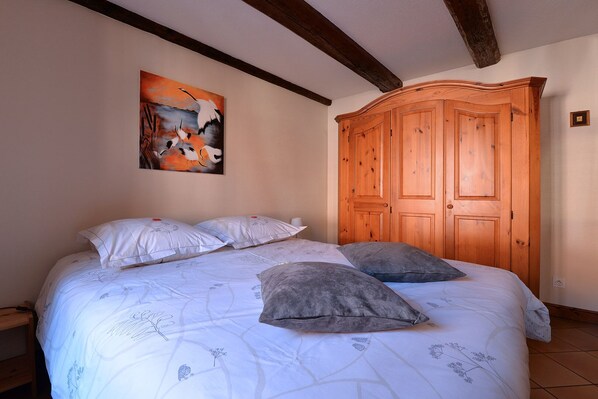Een slaapkamer met een groot bed, twee kussens, een houten garderobe en een schilderij aan de muur.