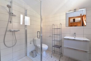 Een moderne badkamer met een douchecabine van glas, een toilet, een wastafel en een metalen schapkas.