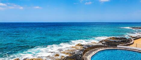 Zona de piscina frente al mar, con vista despejada a la costa rocosa.
