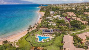 An aerial view of a coastal resort with a swimming pool, beachfront, and dense greenery. - Beachfront Wailea condo w/ direct beach access and pools (Wailea)