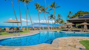 A swimming pool with lounge chairs and umbrellas, palm trees, and a view of a mountain. - Beachfront Wailea condo w/ direct beach access and pools (Wailea)