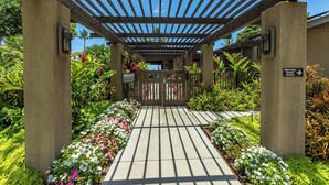 A covered walkway with a gate, surrounded by lush greenery and flowers. - Beachfront Wailea condo w/ direct beach access and pools (Wailea)