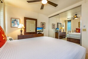 Habitación de hotel con una cama grande, ventilador de techo, televisor y puerta corrediza que da a otra habitación.