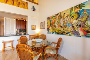 Un comedor con sillas de mimbre y una mesa de vidrio, una cocina con armarios de madera y un mural grande en la pared.