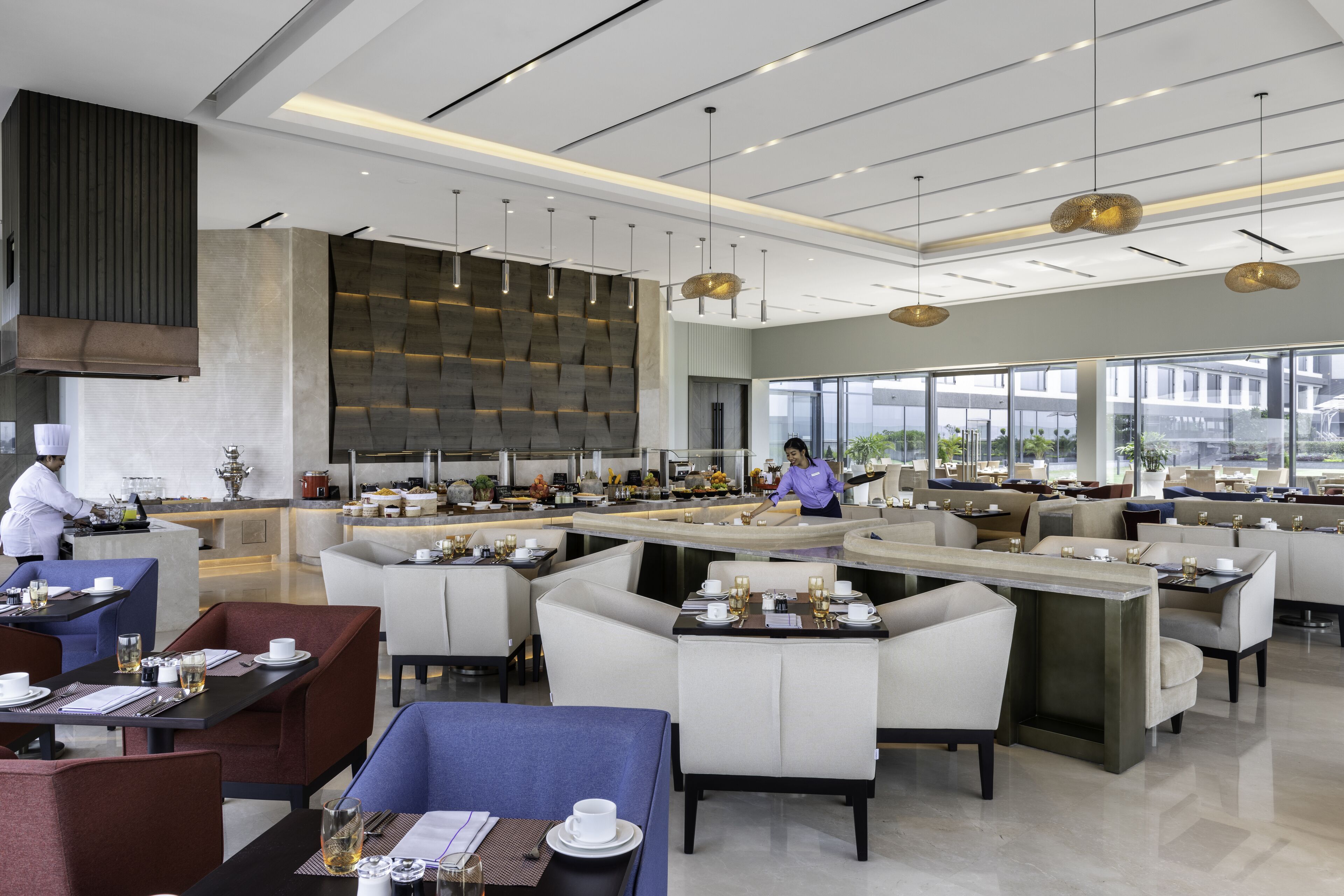 A modern restaurant with a central bar, multiple dining areas, and a view of the city through large windows.
