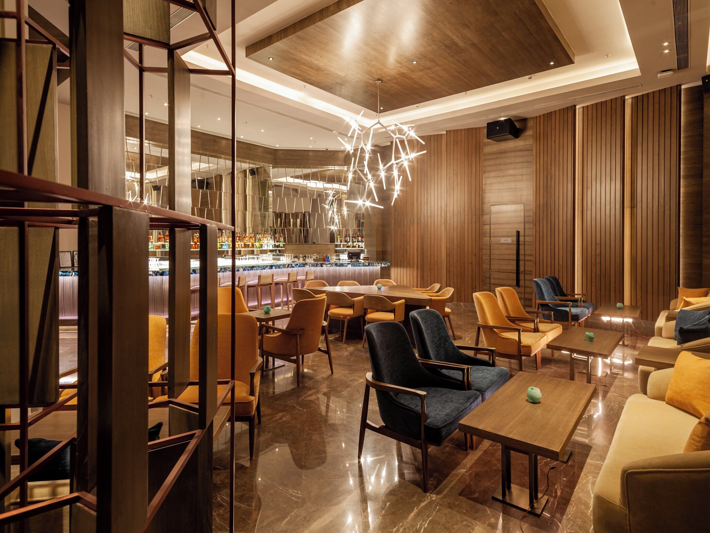 A modern hotel lobby with a bar area, seating arrangements, and a unique geometric light fixture.