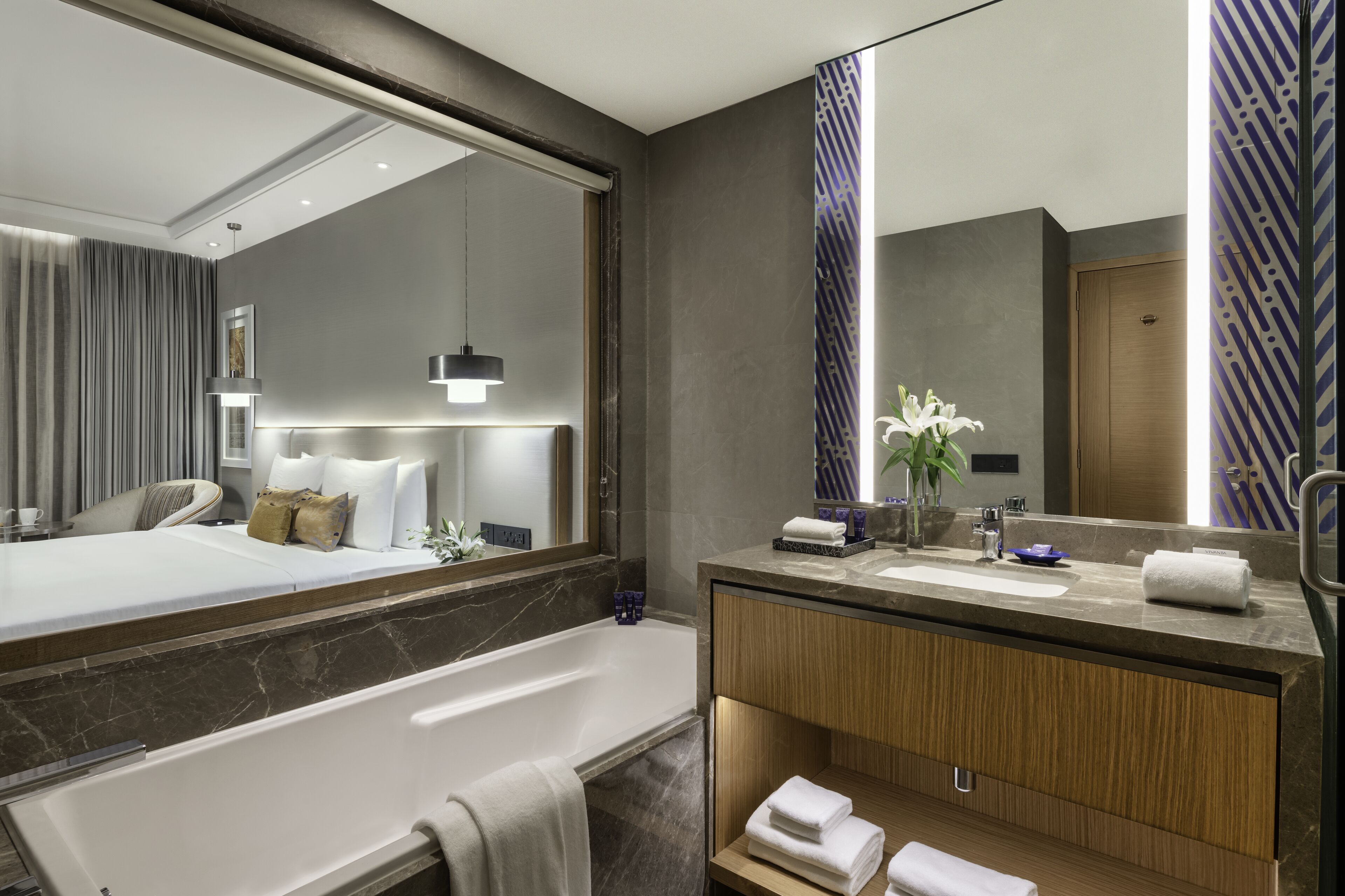 A modern hotel bathroom with a large mirror, a bathtub, a vanity with a sink, and a shower area.