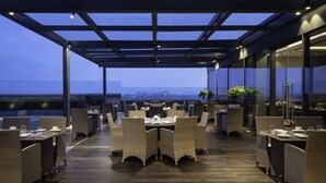 Un área de comedor al aire libre con mobiliario de mimbre y vistas a la ciudad.