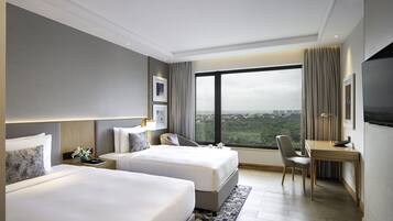 Habitación de hotel con dos camas, un escritorio y un ventanal con vistas a la ciudad.