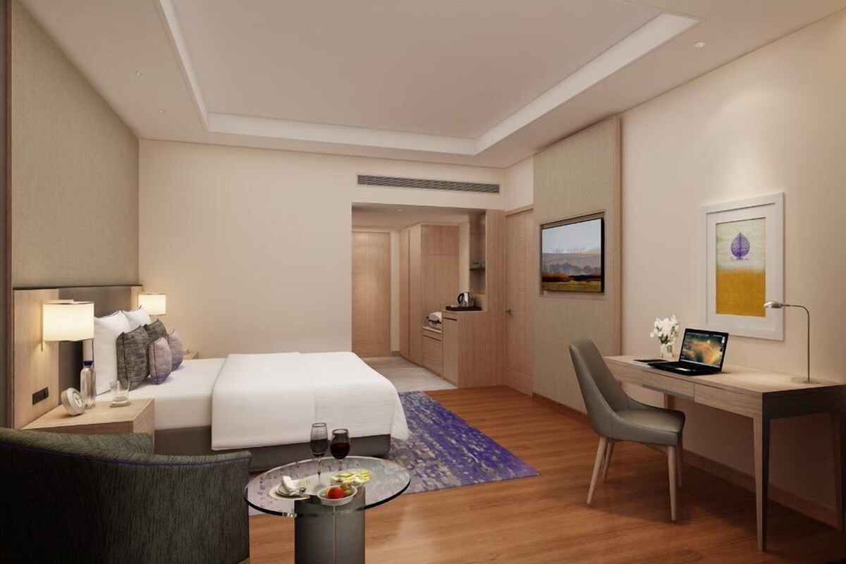 A hotel room with a bed, desk, chair, and a small dining table with food and drinks.