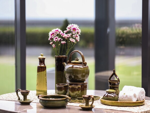 A tea set on a table with a view of a garden through a window.