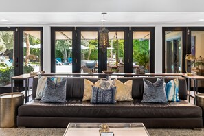 A modern living room with a black leather sofa, a coffee table, and a view of an outdoor pool area.